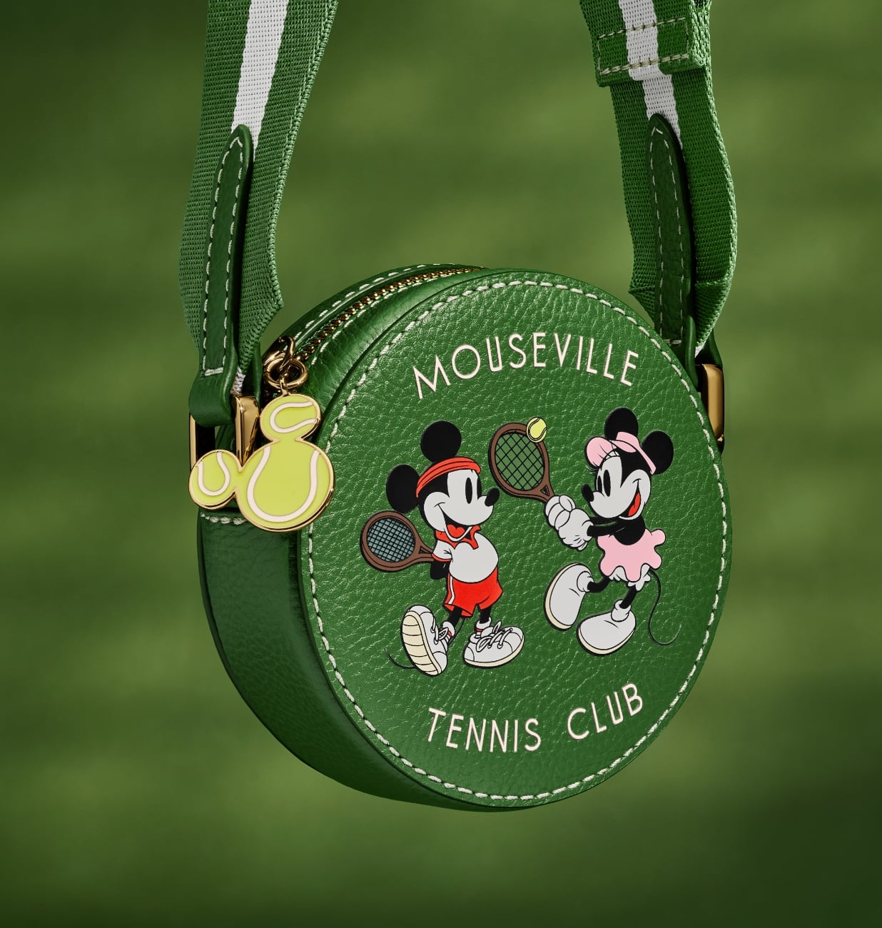 A closeup image of our special-edition mini crossbody handbag, a round silhouette in green leather featuring a screenprinted graphic of Mickey and Minnie playing tennis. 