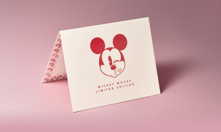 Un GIF de l’emballage en forme de cœur rouge exclusif avec Mickey Mouse envoyant un baiser sur le devant du certificat d’authenticité.