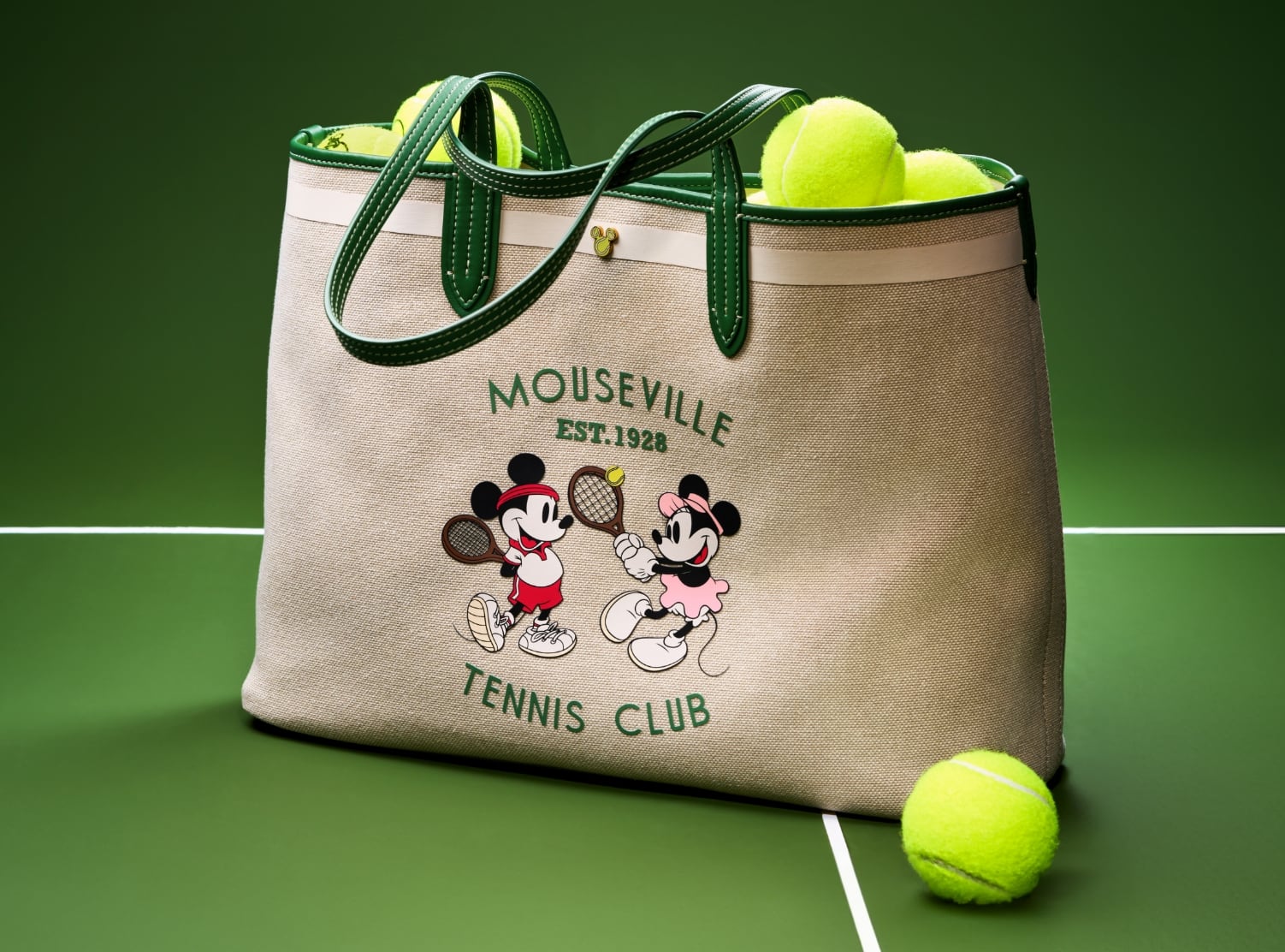 Eine Nahaufnahme unserer Special Edition Mini Crossbody-Handtasche aus grünem Leder mit runder Silhouette und Siebdruckgrafik von Micky und Minnie beim Tennis.