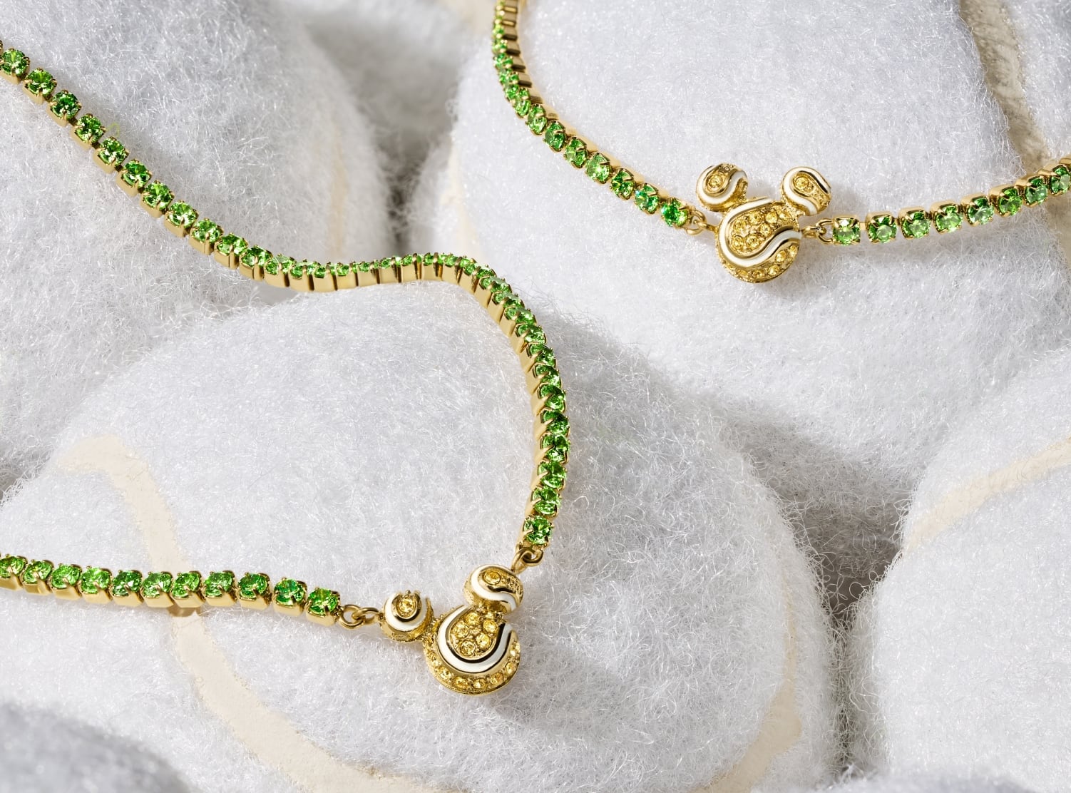 Image shows our Disney Mickey Mouse tennis necklace and bracelet, displayed on white tennis balls. Each piece is embellished with green and yellow pavé crystals. Mickey's silhouette adds a playful accent, reimagined as a trio of sparkling tennis balls.
