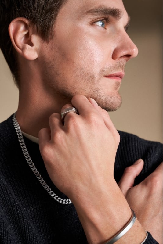 A man in a black shirt wearing silver-tone Fossil jewellery.