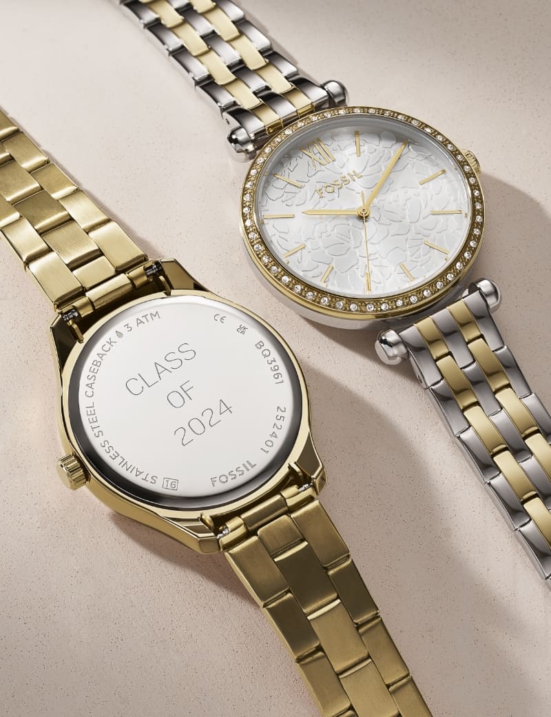 Eine goldfarbene Uhr mit „Class of 2024“-Gravur auf dem Gehäuseboden. Daneben ist eine zweifarbige Damenuhr mit funkelnder Lünette und dezenter Blumenstruktur auf dem Zifferblatt.