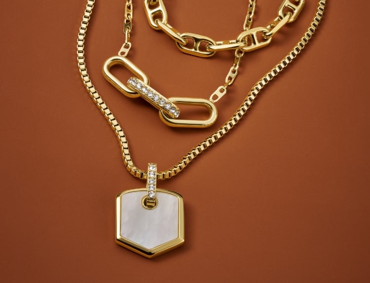 Tre collane color oro della linea di gioielli Fossil Heritage, con dettagli in cristallo e madreperla.
