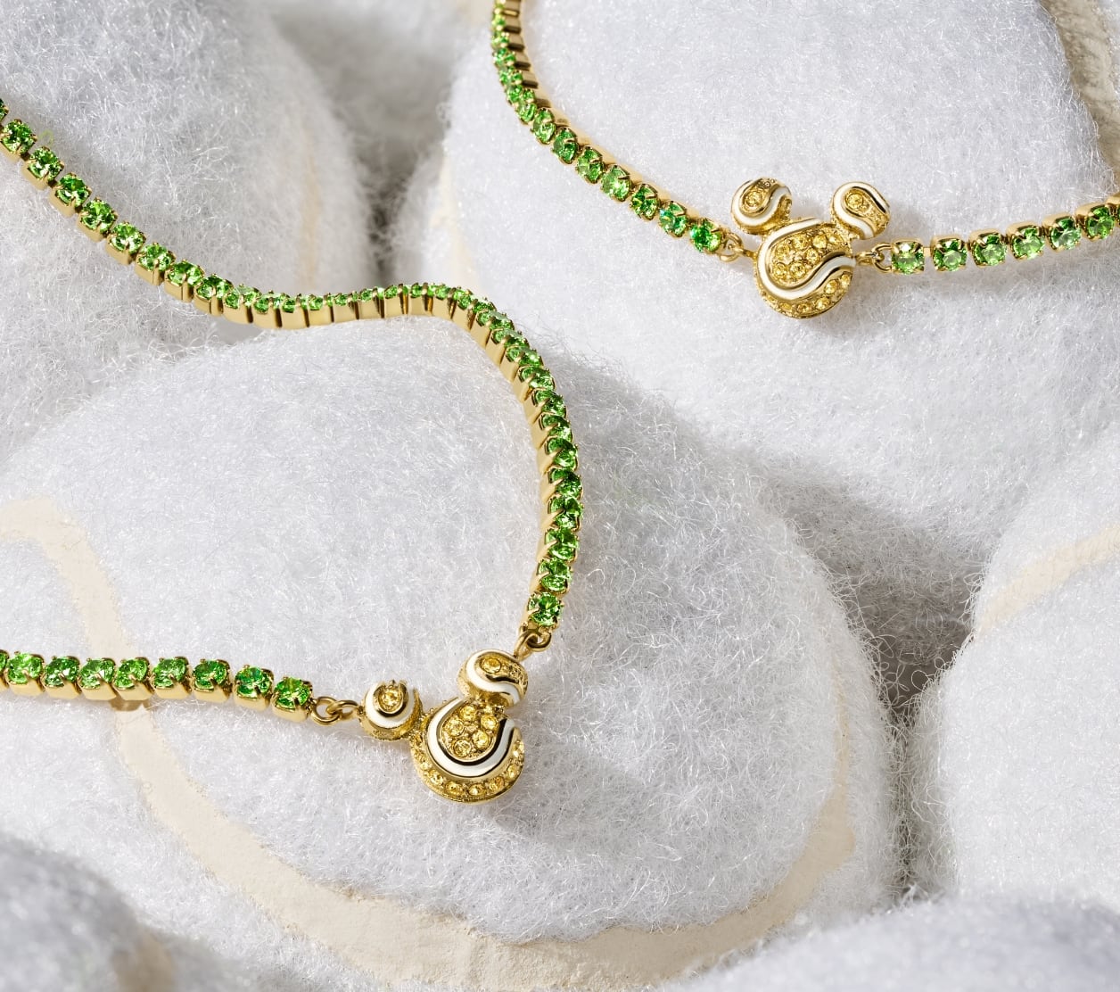 Our Disney Mickey Mouse tennis necklace and bracelet, displayed on white tennis balls. Each piece is embellished with green and yellow pavé crystals. Mickey's silhouette adds a playful accent, reimagined as a trio of sparkling tennis balls.