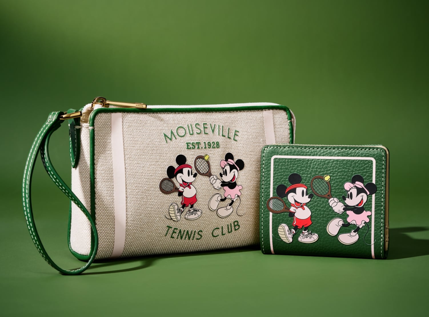 Our special-edition Disney Tennis wristlet and bifold wallet, shown side by side on a tennis court green background. The wristlet is crafted of cotton canvas with green leather trim. It features a screenprinted graphic of Mickey and Minnie playing tennis with the text 'Mouseville Tennis Club, Est. 1928.' The bifold wallet is screenprinted with the same custom graphic on rich green leather.
