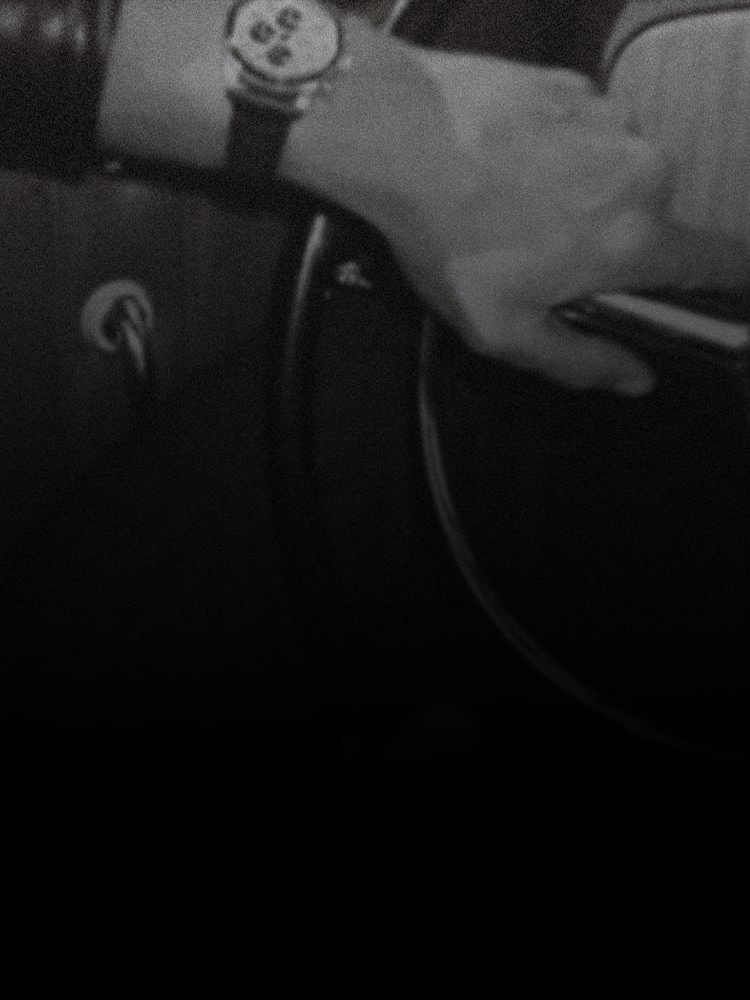 Image d’arrière-plan en noir et blanc d’un homme portant une montre et conduisant une voiture d’époque.
