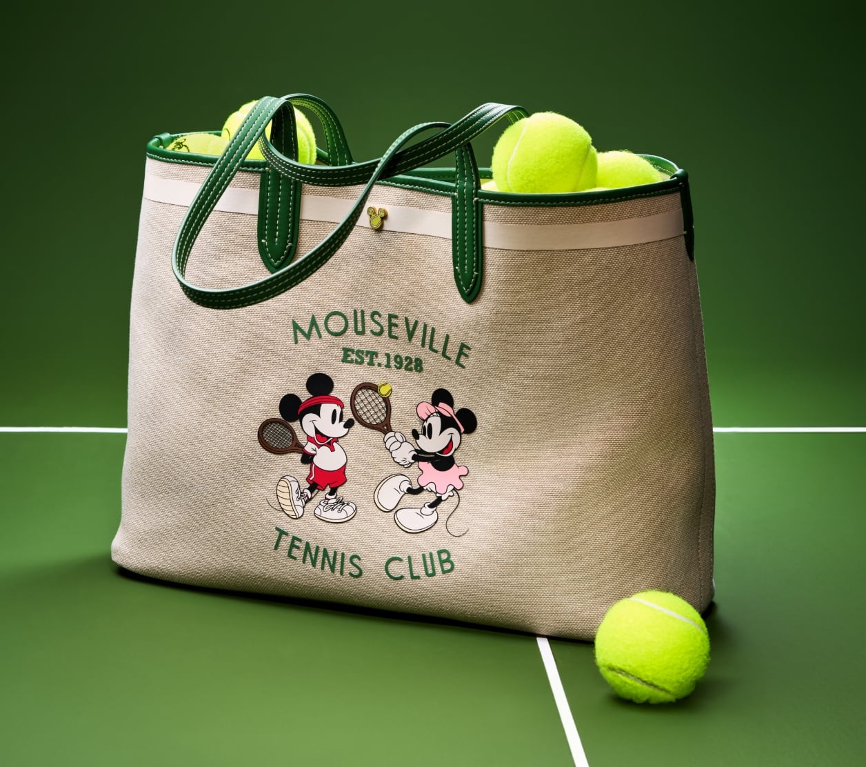 Our special-edition Disney Tennis tote, filled with bright green tennis balls and showcased on a tennis court. Crafted of cotton canvas with green leather trim, the bag features a screenprinted graphic of Mickey and Minnie playing tennis with the text 'Mouseville Tennis Club, Est. 1928.'